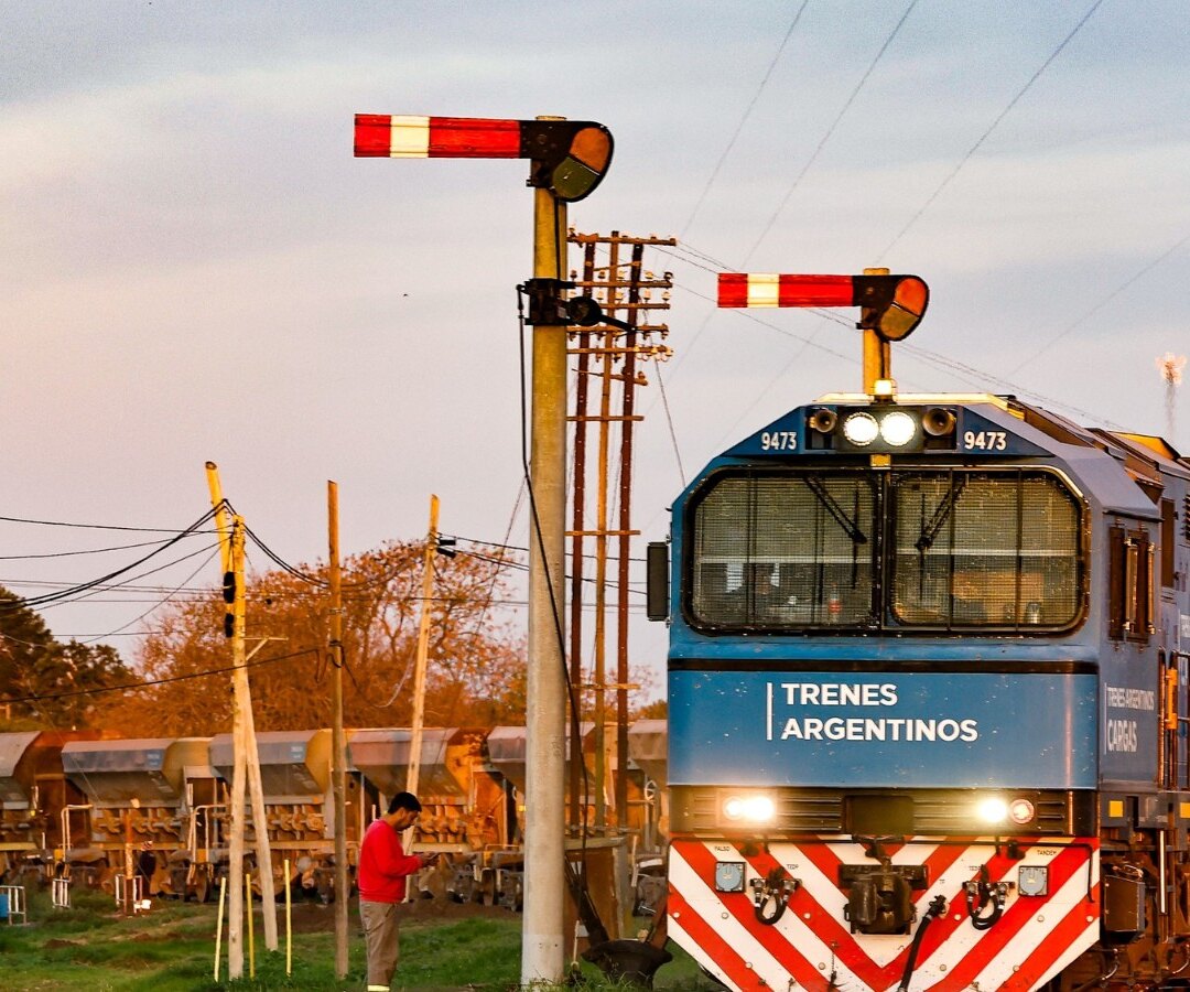 Locomotora de Trenes Argentinos Cargas detenida junto a vagones tolva y señales ferroviarias al atardecer