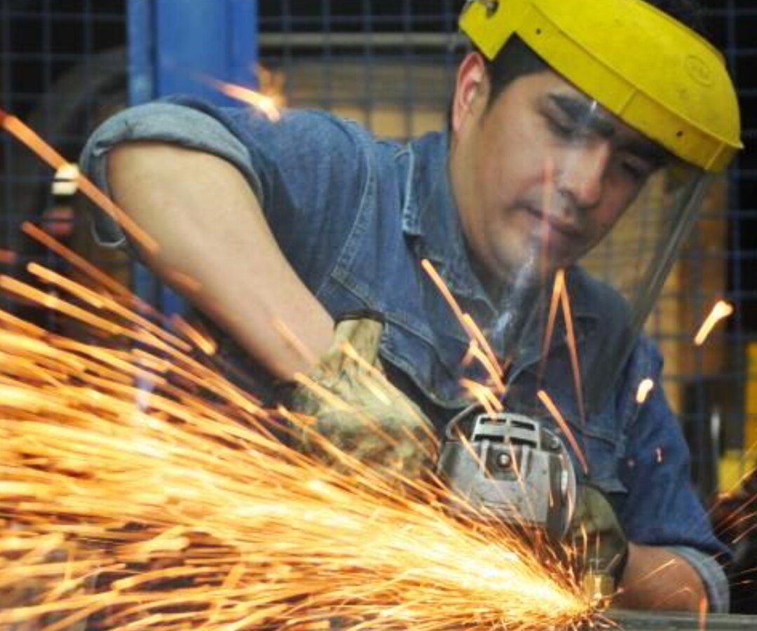 Trabajador con máscara de protección amola una pieza de metal en un taller mientras saltan chispas