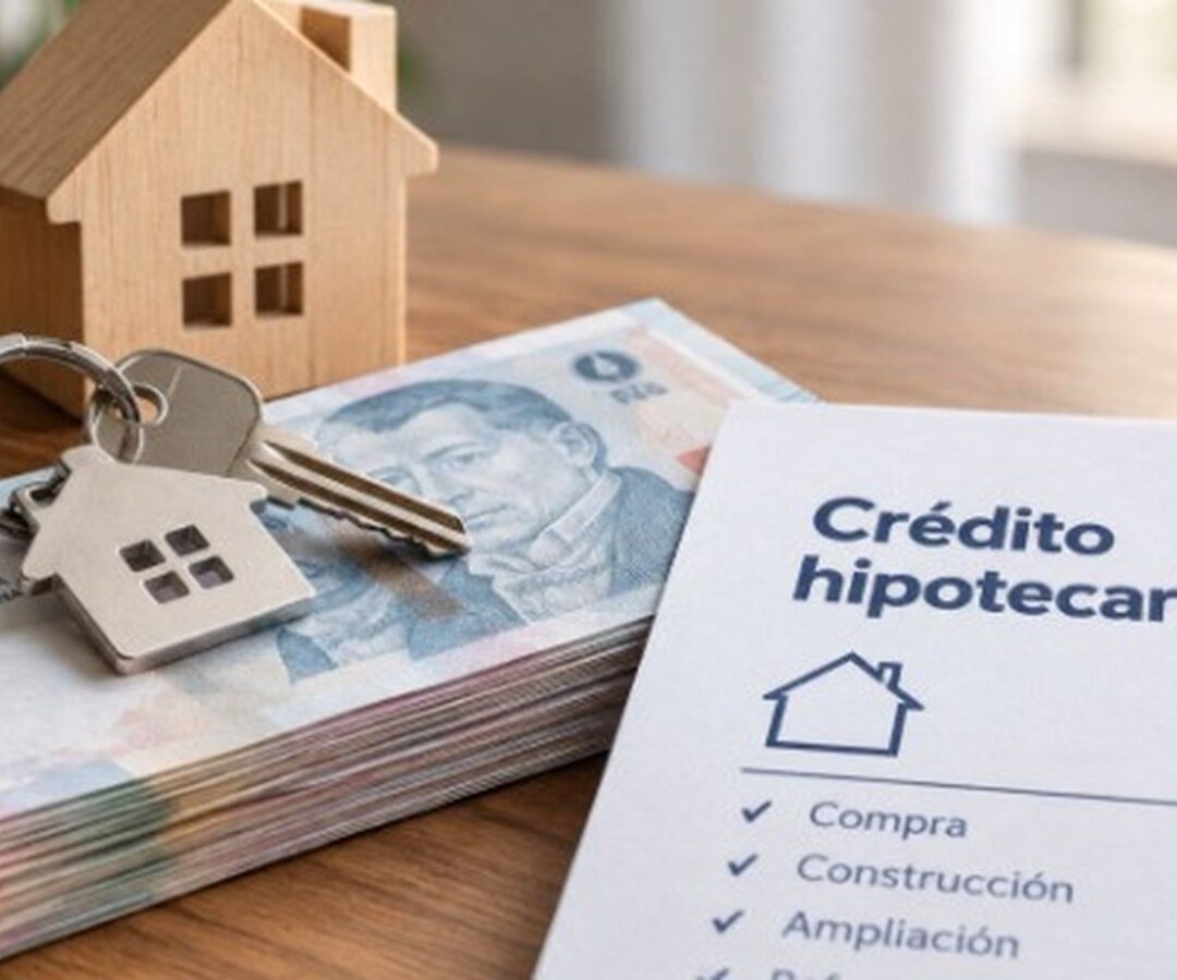Llavero con forma de casa sobre billetes de diez mil pesos junto a un formulario de crédito hipotecario UVA