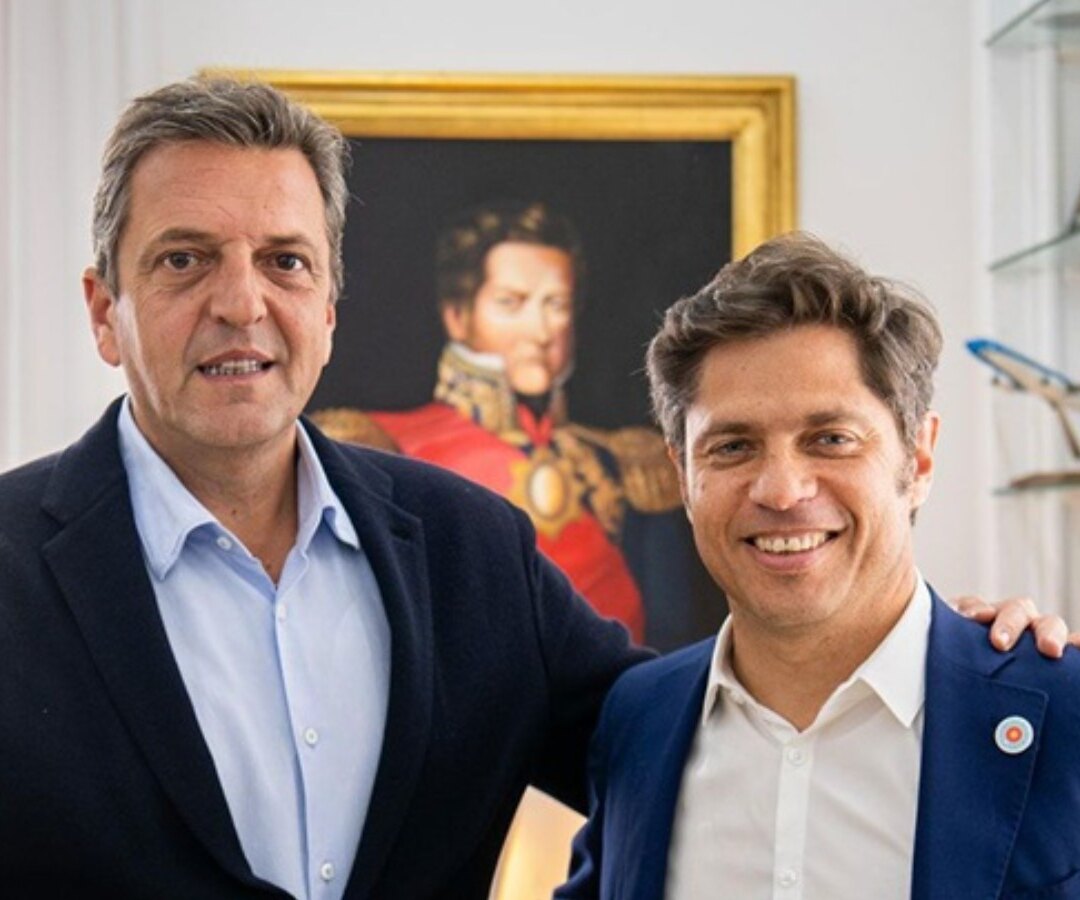 Dos dirigentes peronistas posan sonrientes y abrazados en un despacho, con un retrato militar del siglo XIX de fondo