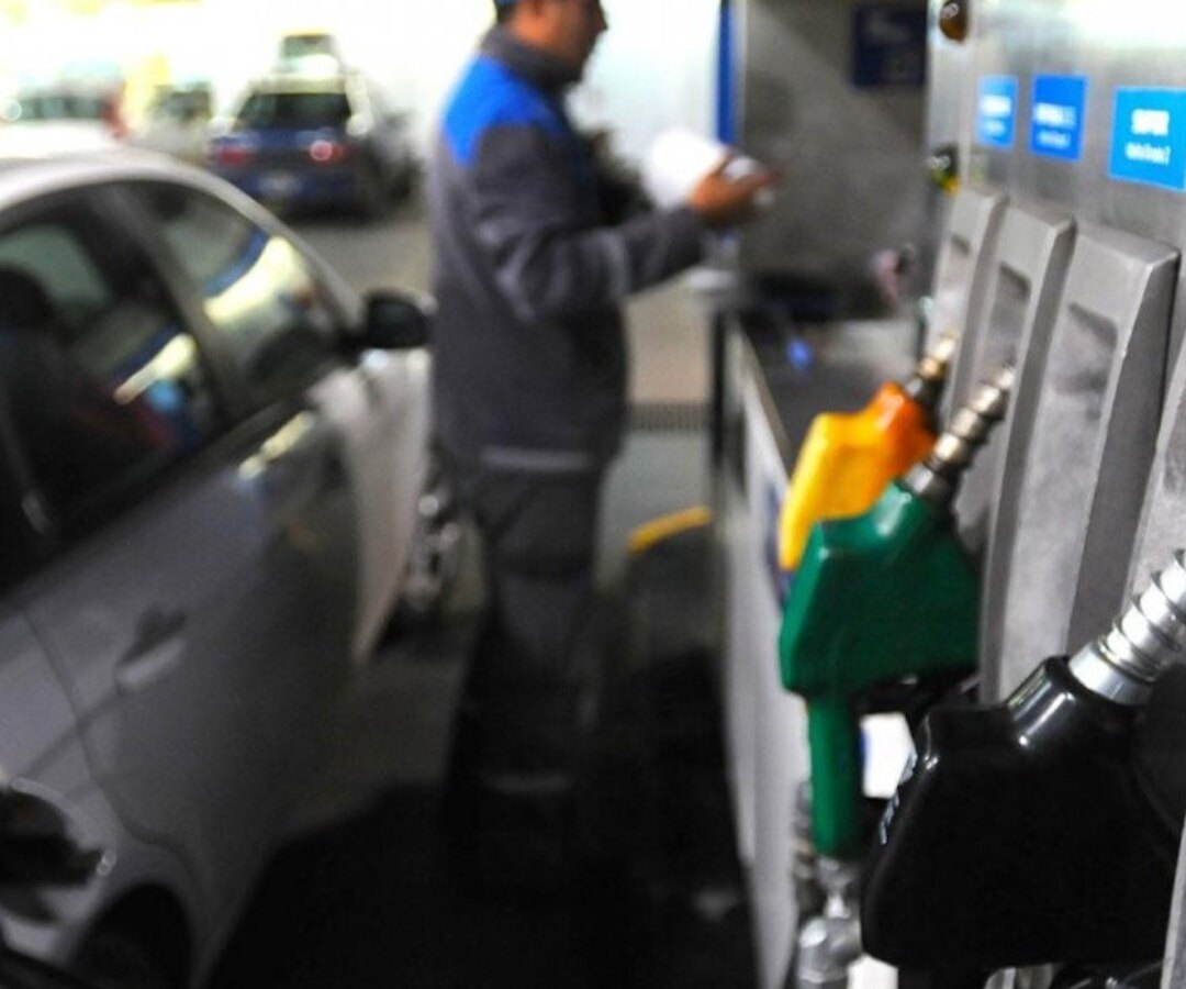 Playero junto a los surtidores de una estación de servicio mientras un auto carga combustible