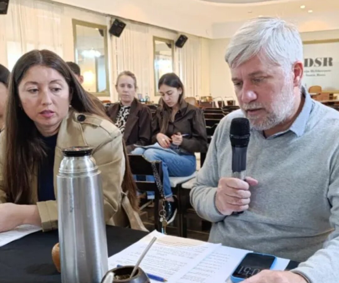 Reunión de comisión en el Concejo Deliberante de Santa Rosa: un hombre habla por micrófono junto a papeles, termo y mate